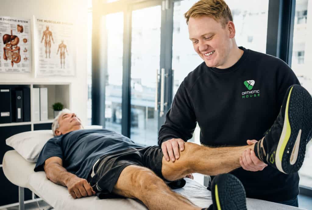 Orthotic House orthotist assessing an older patient's knee and leg during a clinical consultation.